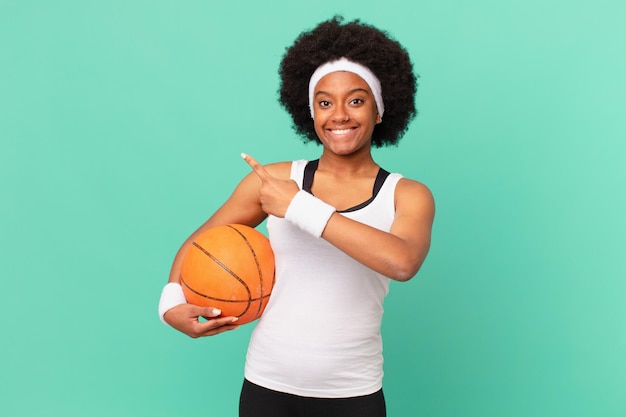 Afro woman looking excited and surprised pointing to the side and upwards to copy space. basketball concept