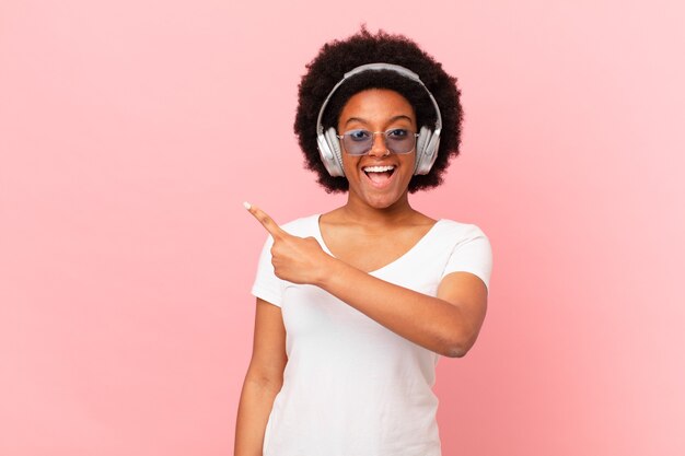 Afro woman looking excited and surprised pointing to the side and upwards to copy space. music concept