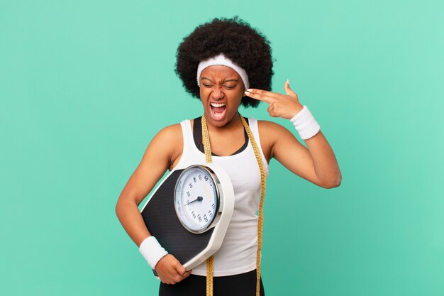 Afro woman looking unhappy and stressed, suicide gesture making gun sign with hand, pointing to head diet concept