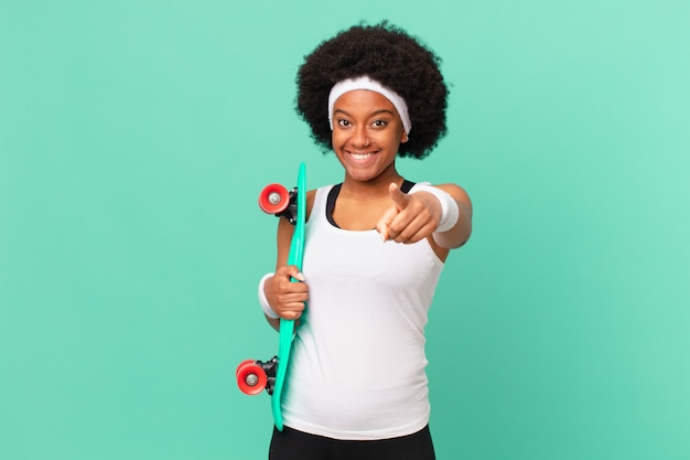 Afro woman pointing at camera with a satisfied, confident, friendly smile, choosing you. skateboard concept