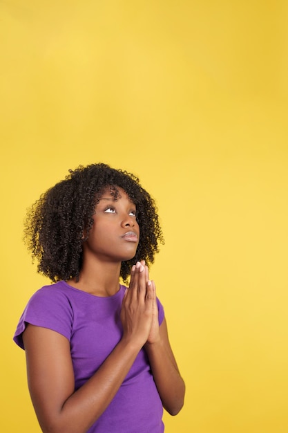 Afro woman praying while looking up joining hands