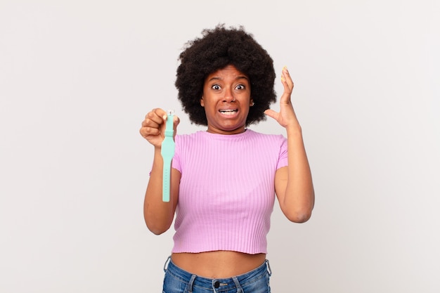 Afro woman screaming with hands up in the air, feeling furious, frustrated