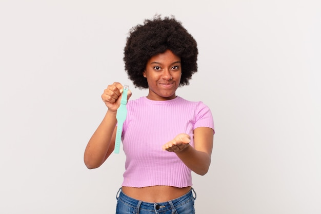 Afro woman smiling happily with friendly, confident, positive look, offering and showing an object or concept watch concept