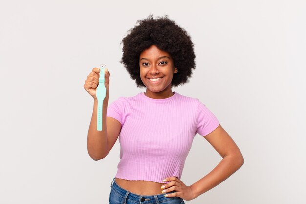 Afro woman smiling happily with a hand on hip and confident, positive, proud and friendly attitude watch concept