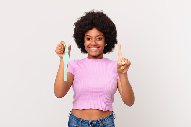 Afro woman smiling and looking friendly, showing number one or first with hand forward, counting down watch concept