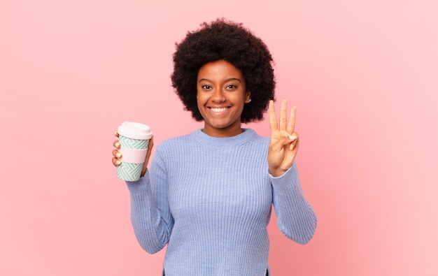 Afro woman smiling and looking friendly, showing number three or third with hand forward, counting down. coffee concept