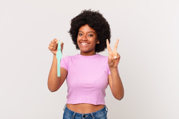 Afro woman smiling and looking friendly, showing number two or second with hand forward, counting down watch concept