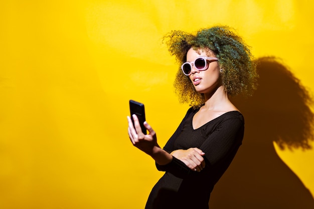 Photo afro woman takes selfie with sun glasses on yellow background