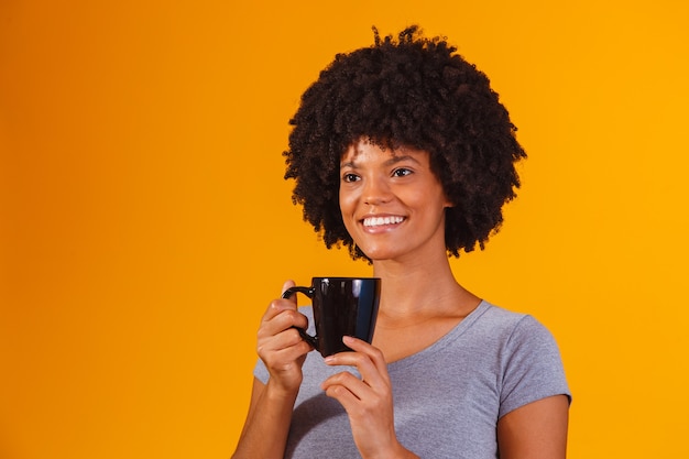 Afro woman taking tea on yellow