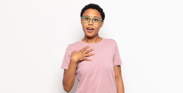 Afro young black woman feeling shocked, astonished and surprised, with hand on chest and open mouth, saying who, me?