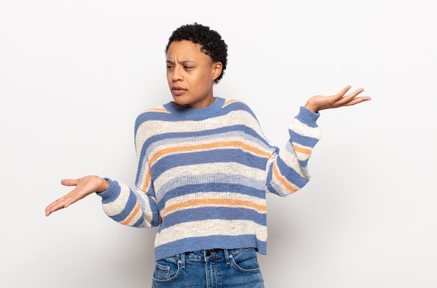 Afro young black woman looking puzzled, confused and stressed, wondering between different options, feeling uncertain