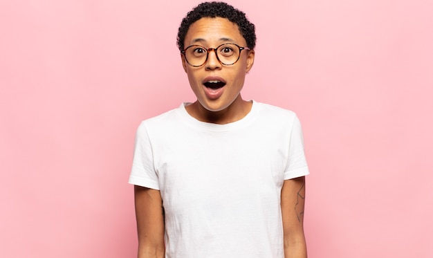 Afro young black woman looking very shocked or surprised, staring with open mouth saying wow