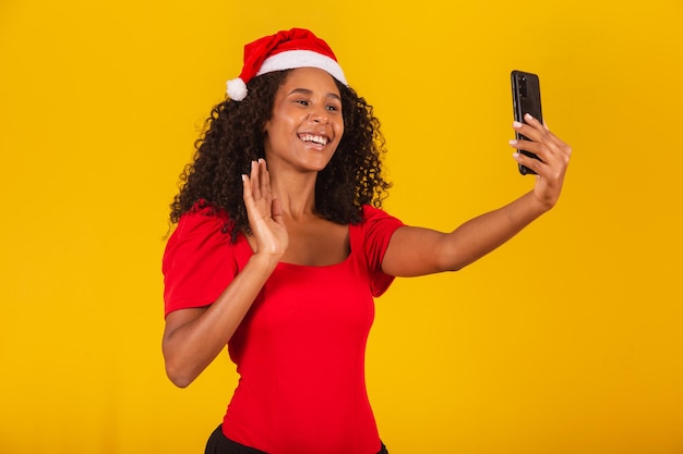 Afro young man in Christmas hat making video call on yellow background.