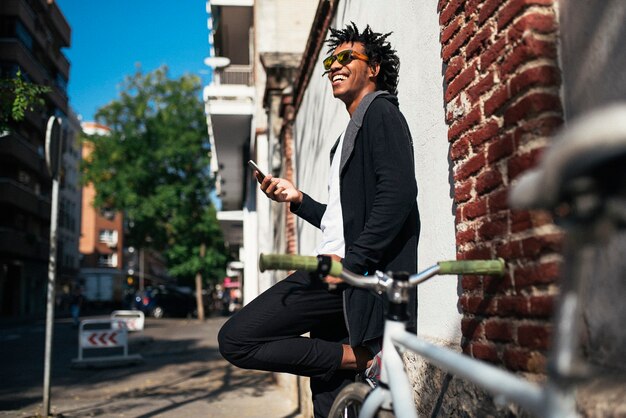 Afro young man using mobile phone and fixed gear bicycle in the street.