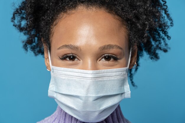 Photo afro young woman with curly hair looking at camera wears protective medical mask being on quarantine