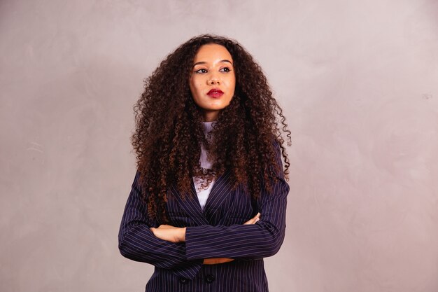 Afro zakenvrouw met gekruiste armen camera kijken over grijze achtergrond.