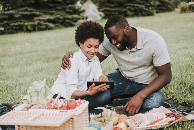 Afro Zoon en vader op zoek op tablet op picknick