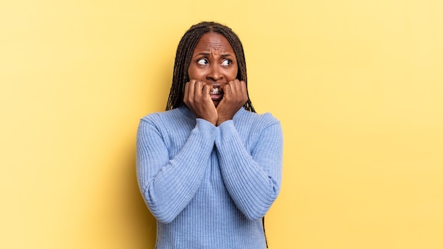 Afro-zwarte mooie vrouw die bezorgd, angstig, gestrest en bang kijkt, vingernagels bijt en op zoek is naar laterale kopieerruimte