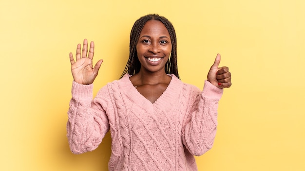 Afro-zwarte mooie vrouw die lacht en er vriendelijk uitziet, nummer zes of zesde toont met de hand naar voren, aftellend