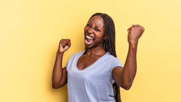 Afro-zwarte mooie vrouw die triomfantelijk schreeuwt, eruitziet als een opgewonden, blije en verraste winnaar, vierend