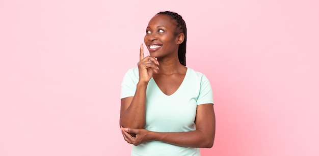 Afro zwarte volwassen vrouw die vrolijk lacht en zijwaarts kijkt, zich afvraagt, denkt of een idee heeft