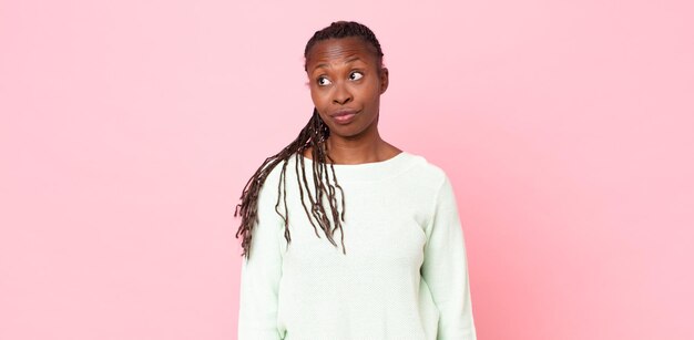 Afro zwarte volwassen vrouw die zich afvraagt, gelukkige gedachten en ideeën denkt, dagdroomt, op zoek is naar ruimte aan de zijkant te kopiëren