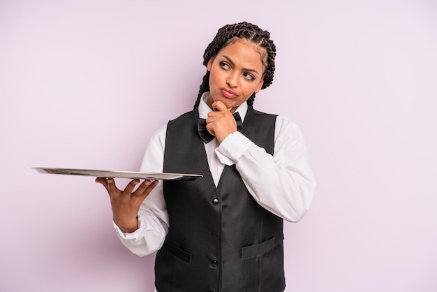 Afro zwarte vrouw denkt, voelt zich twijfelachtig en verward. ober met een dienblad