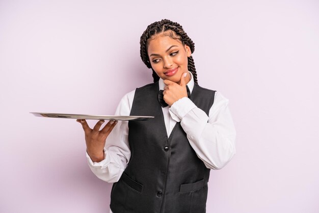 Afro-zwarte vrouw die lacht met een vrolijke zelfverzekerde uitdrukking met de hand op de kin Ober met een dienblad