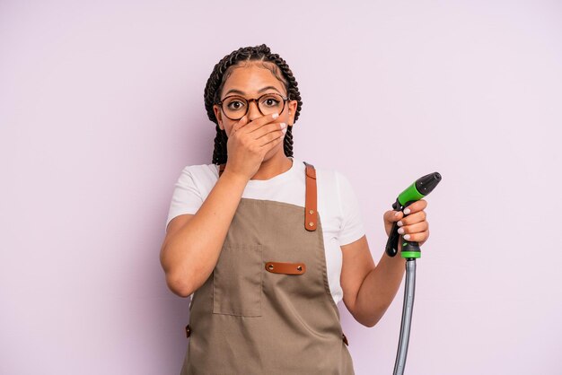 Afro zwarte vrouw die mond bedekt met handen met een geschokt. tuinman slang concept