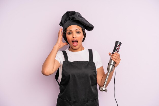 Afro zwarte vrouw schreeuwen met handen omhoog in de lucht chef-kok met staafmixer