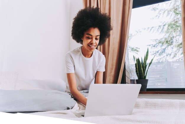 Afroamerican girl resting in bed at home  Beautiful woman relaxing at home and using computer laptop