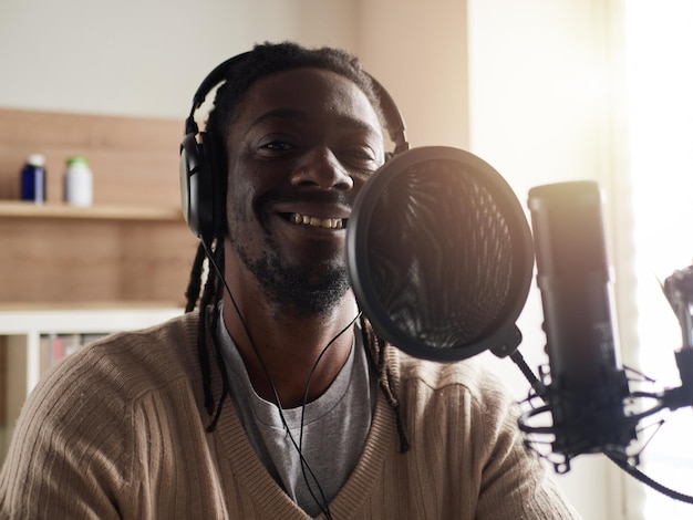 Афроамериканский счастливый молодой мужчина записывает аудиоблог в наушниках, транслирует микрофон дома