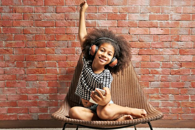 Photo afroamerican little girl with headphones and phone on brick wall background