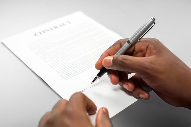 Afroamerican male signs loan contract. Just sign the paper. Beware of small font. Remember the deadline.