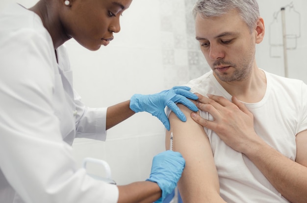 An AfroAmerican nurse vaccinates a patient with a syringe in a medical office