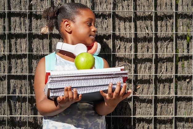 Afroamerican school girl with backpack headphones and books at school entrance