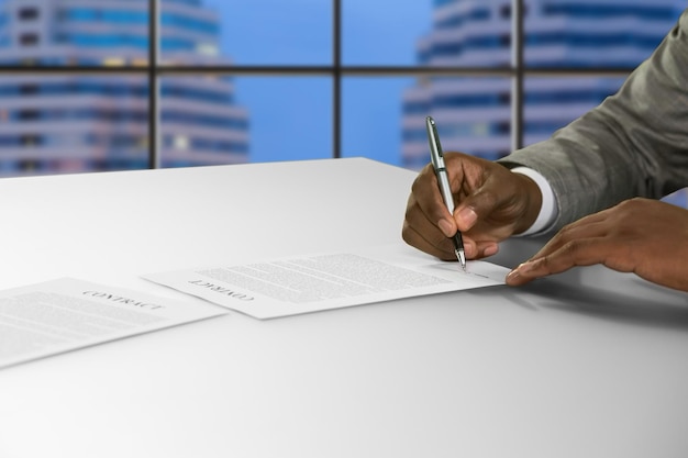 Афроамериканец подписывает документ в офисе. Черный бизнесмен, подписывающий контракт. Вечер в центре занятости. Корпоративный шпионаж в городе.