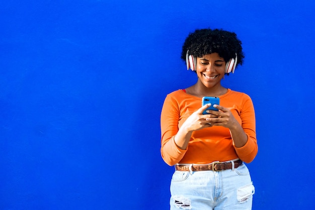 Afroamerican woman with orange sweater and white headphones taking a mobile