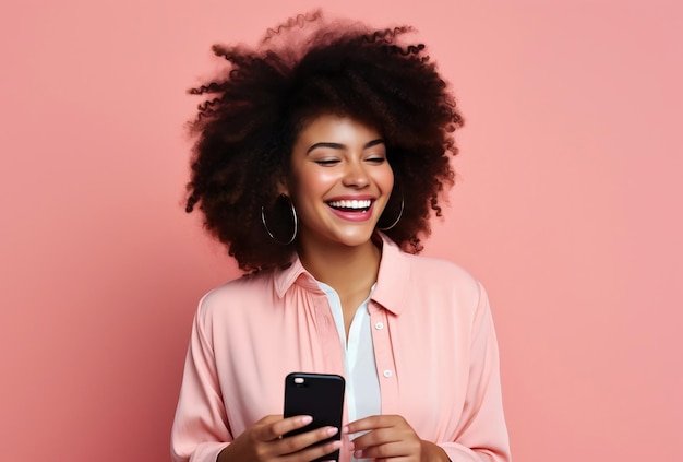 Афроволосая молодая женщина счастливо держит мобильный телефон на розовом фоне