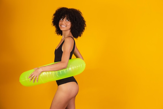 Afrovrouw met zwart machtshaar die een drijvende boei op gele achtergrond gebruiken. vakantie concept