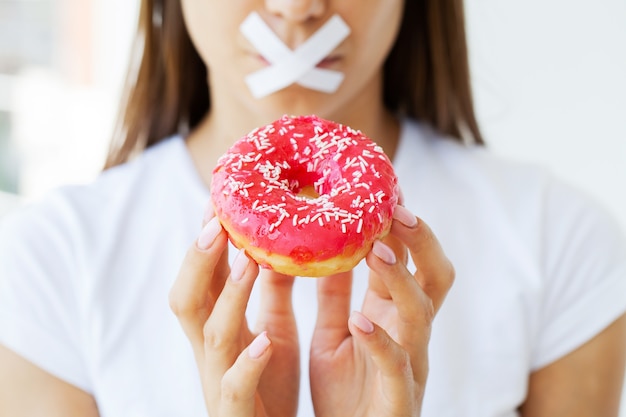 Afslankconcept, jonge vrouw met verzegelde mond die junkfood opgeeft.