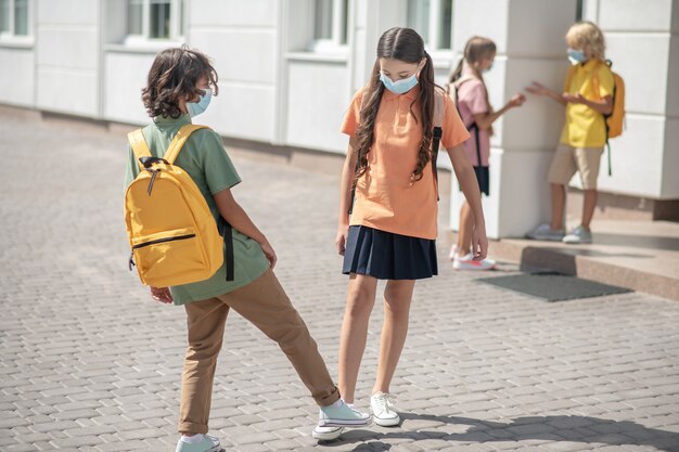 Afstand houden. Schoolkinderen in beschermende maskers op het schoolplein begroeten elkaar en houden afstand