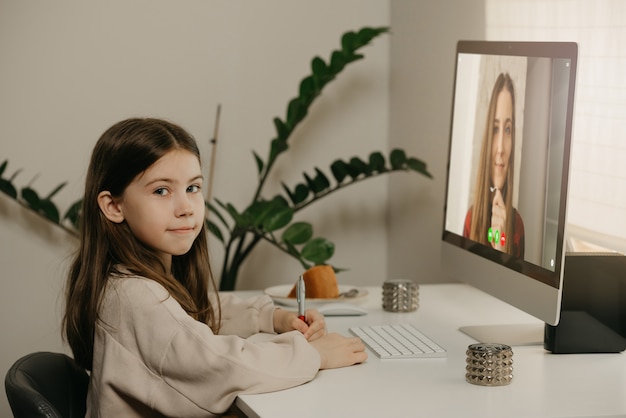 Afstand leren. Een jong meisje met lang haar op afstand studeren van haar mannelijke leraar online. Een mooi vrouwelijk kind leert thuis een les met een desktopcomputer. Thuisonderwijs.