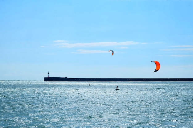 Afstandsbeeld van mensen die kiteboarden in de zee tegen een blauwe lucht