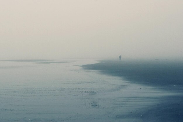 Foto afstandsbeelding van een persoon die bij mistig weer op het strand staat