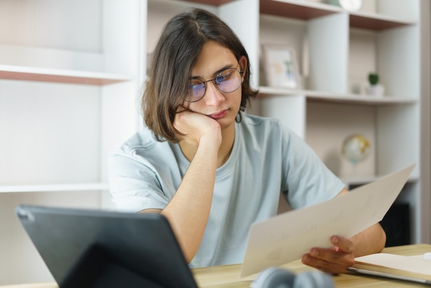 Afstandsonderwijs concept De tienerjongen leest grafiek op document en studeert online klasse op tablet