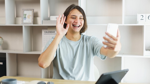 Afstandsonderwijs concept Tienerjongen maakt gebaar naar begroeting met klasgenoot op smartphone