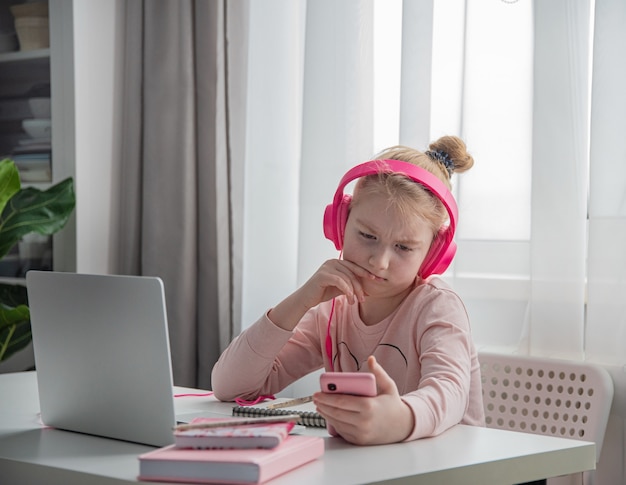Afstandsonderwijs. een schoolmeisje met een roze koptelefoon studeert huiswerk tijdens hun online les thuis via internet. sociale afstand tijdens quarantaine