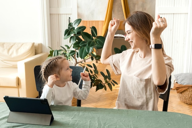 Afstandsonderwijs Moeder met haar dochtertje die thuis online leert tijdens de covid19-pandemie Moeder en baby zijn blij dat ze hun huiswerk in de kamer hebben gemaakt met behulp van een tablet