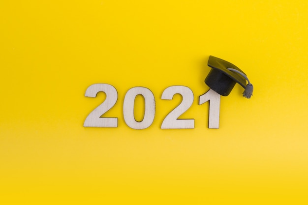 Afstuderen 2021. Houten nummer 2021 met afgestudeerde hoed op gele achtergrond bovenaanzicht.